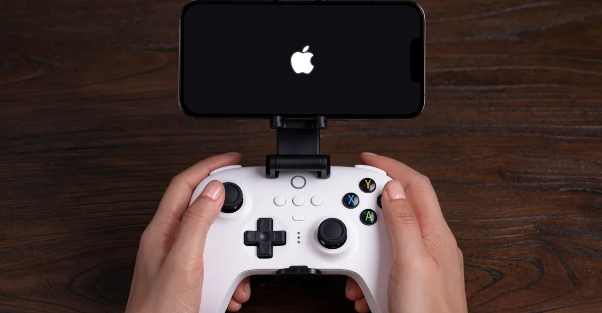 Hands hold a white game controller attached to an iPhone displaying the Apple logo.