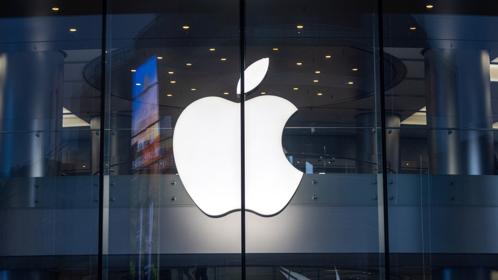 A bright white Apple logo is visible behind glass panels in a dimly lit building.
