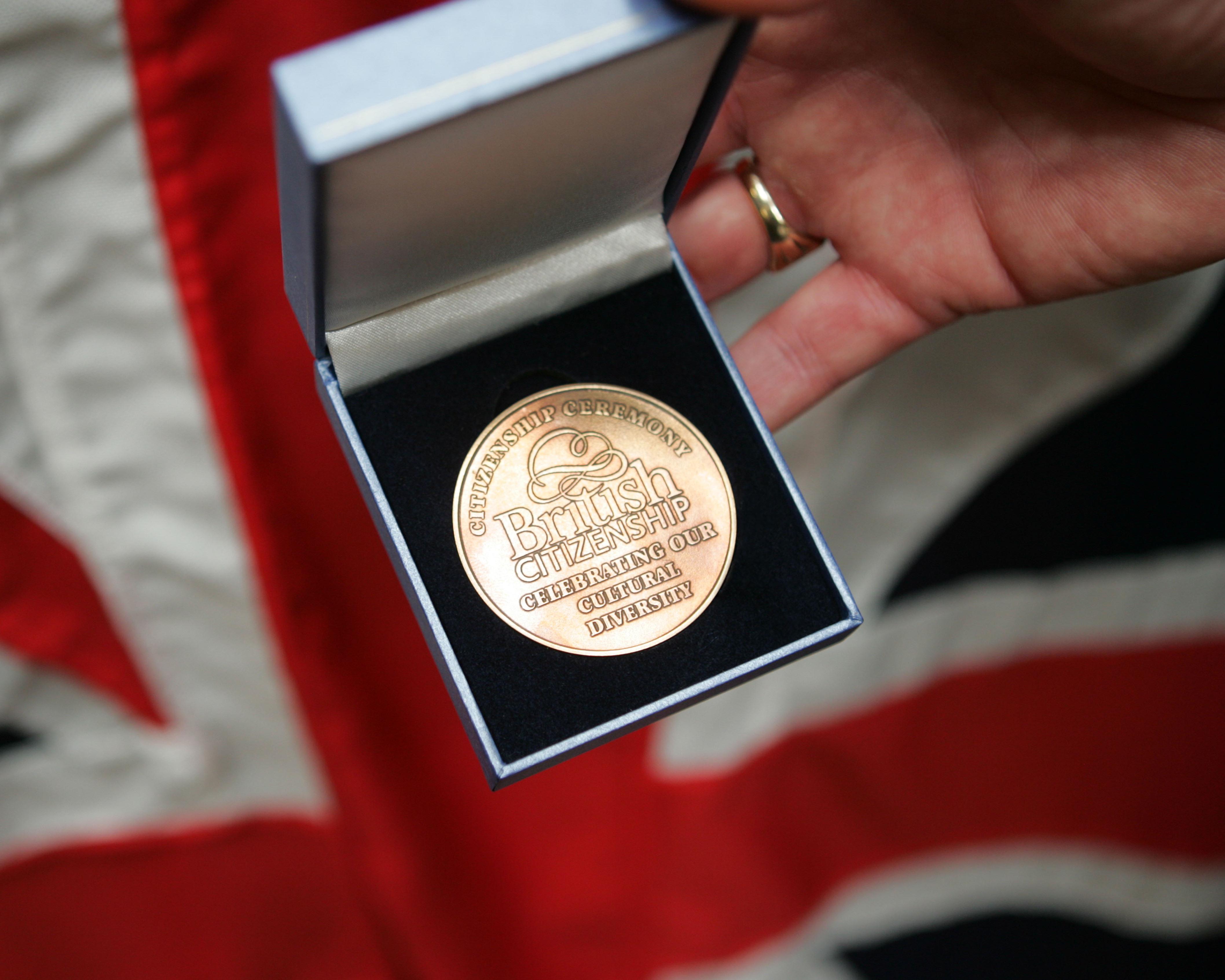 Hand holds an open presentation box containing a British citizenship ceremony medal.