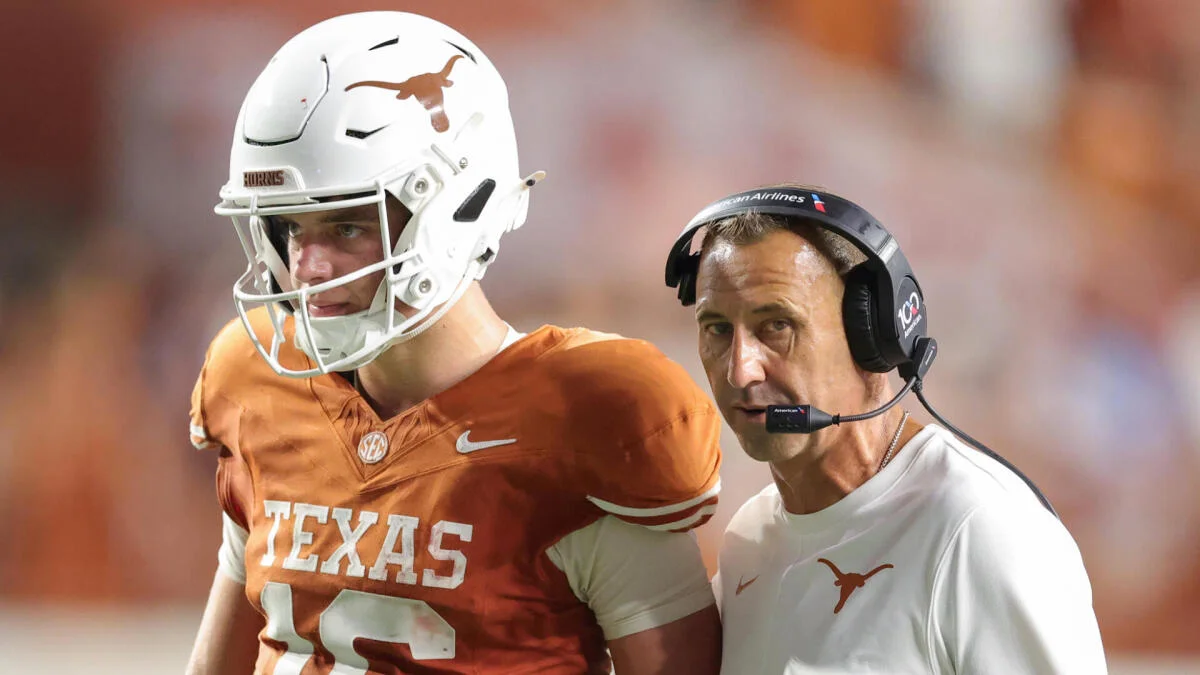 Texas football player in helmet stands beside a coach wearing a headset on the sideline.