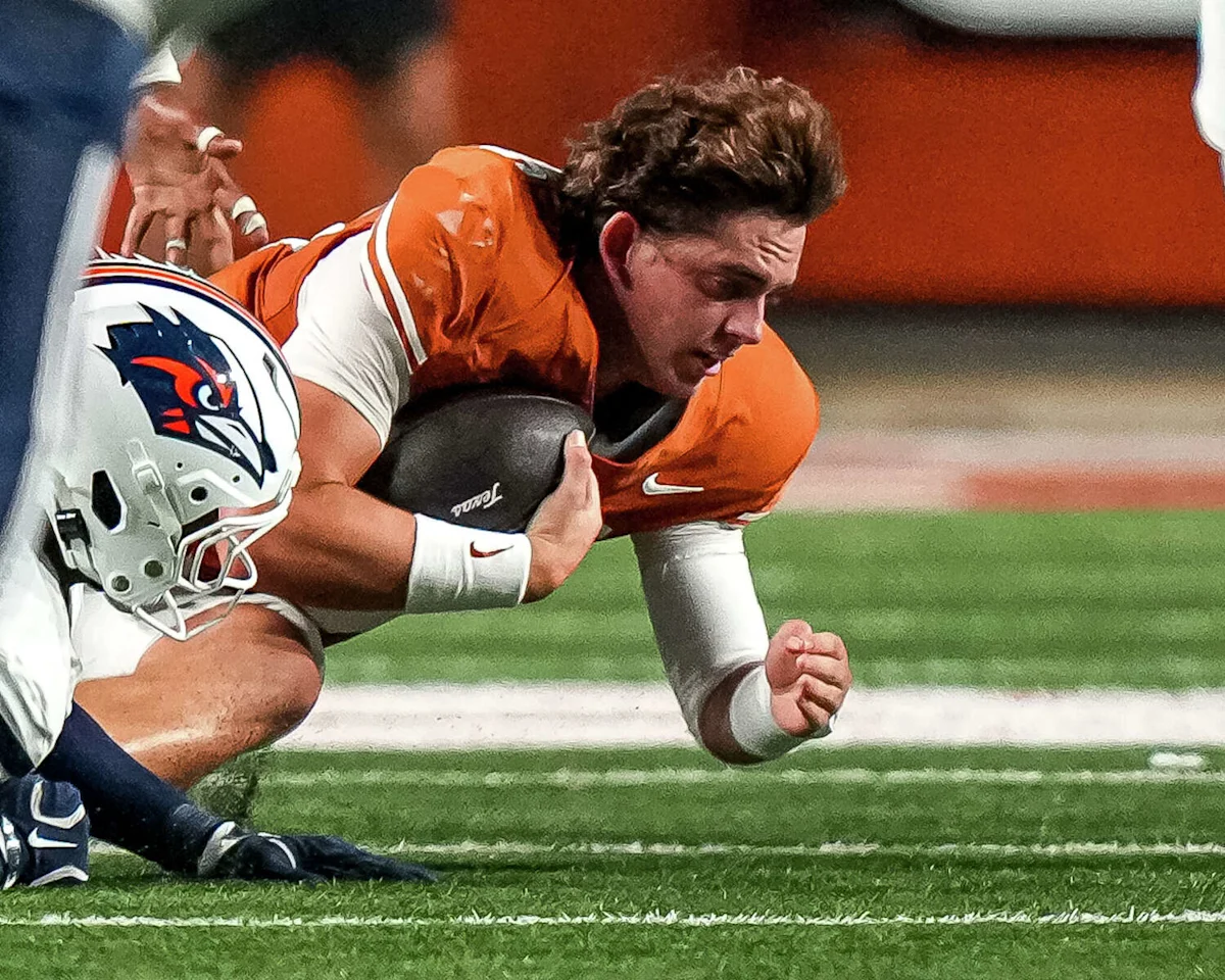 Football player in an orange jersey clutches the ball while being tackled near the sideline.