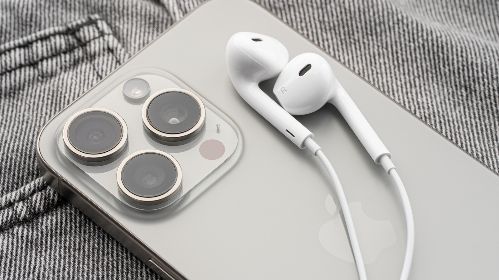 White wired EarPods resting on the back of a silver smartphone beside its triple-camera module