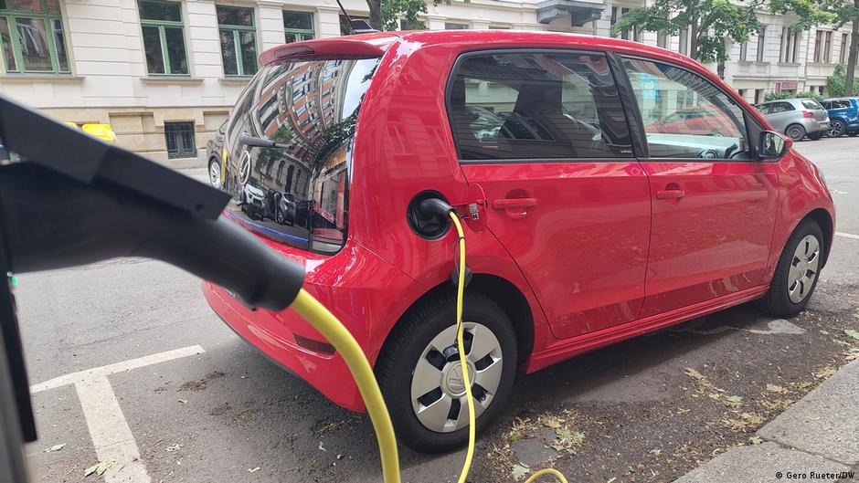 A red electric car charges beside a curb, with a yellow cable connected to its rear.