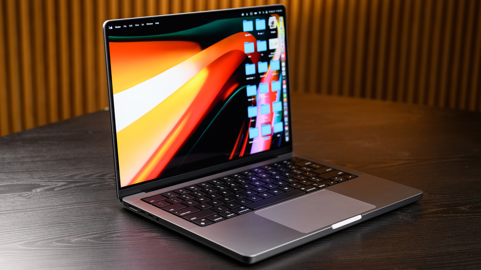 Open MacBook displaying a colorful desktop on a dark wooden table