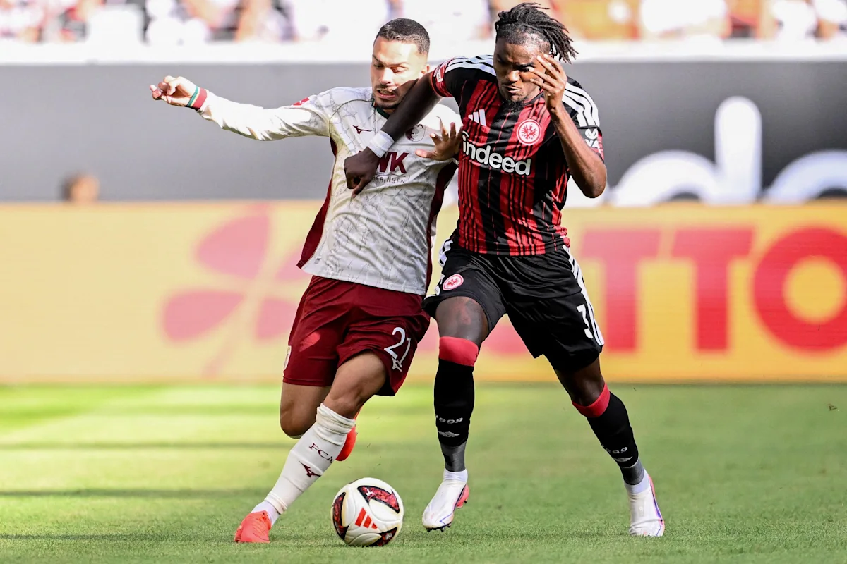 Two footballers in opposing kits compete for the ball during a match.