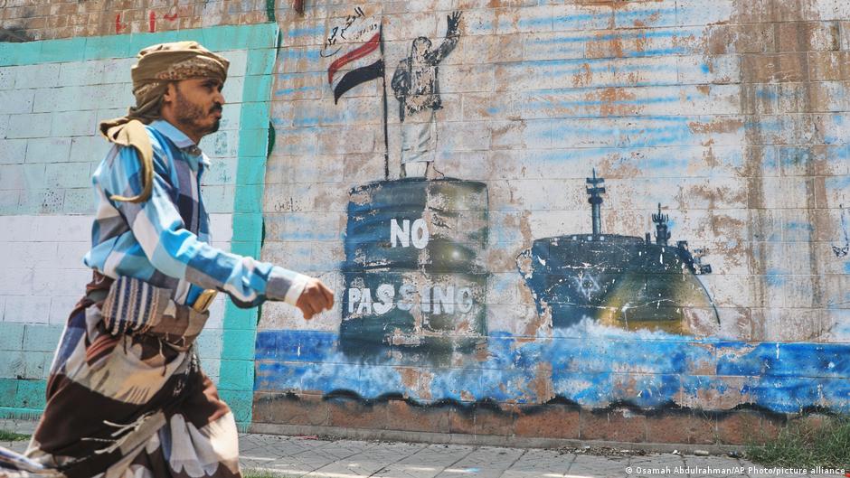 A man walks past a weathered mural depicting a ship and the words “No Pasaran.”