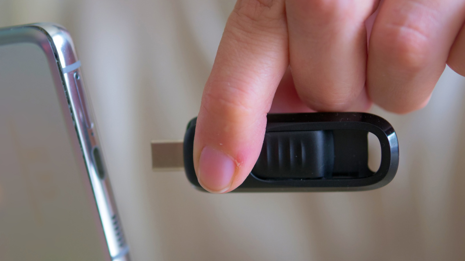Hand plugging a black USB flash drive into a smartphone beside another phone.