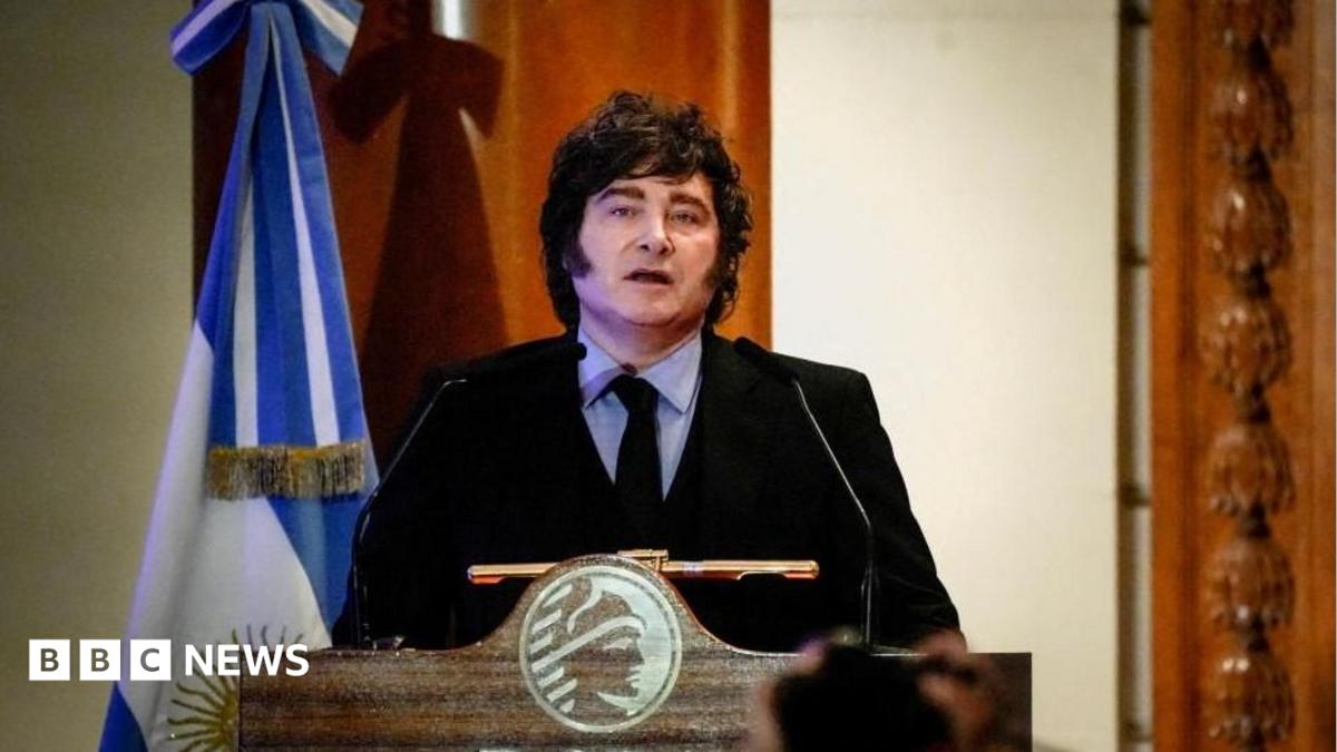 Man speaking at a lectern beside an Argentine flag during a formal event