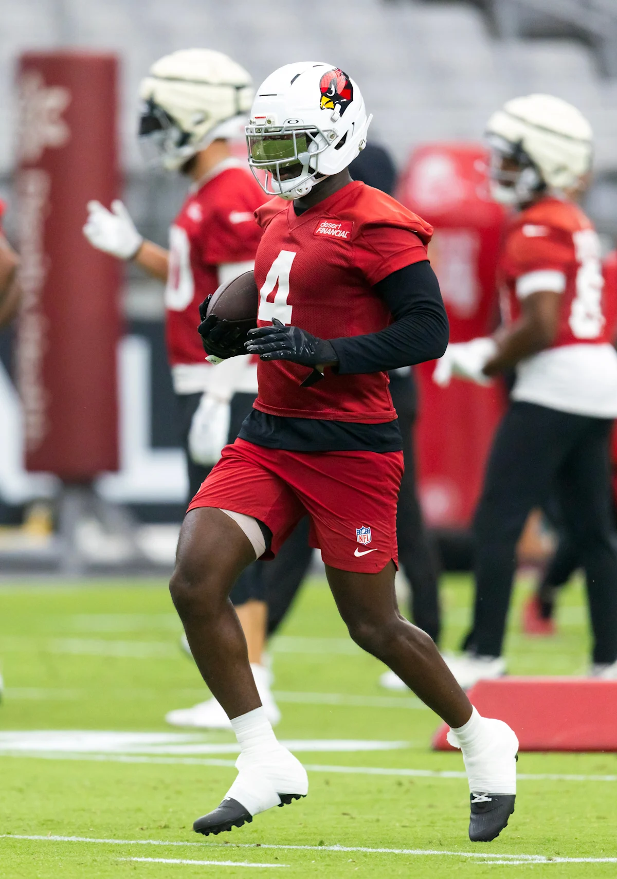Arizona Cardinals running back in red uniform carries a football during practice.