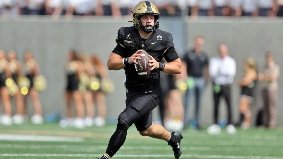 Football player in a dark uniform and gold helmet runs with the ball on a field.
