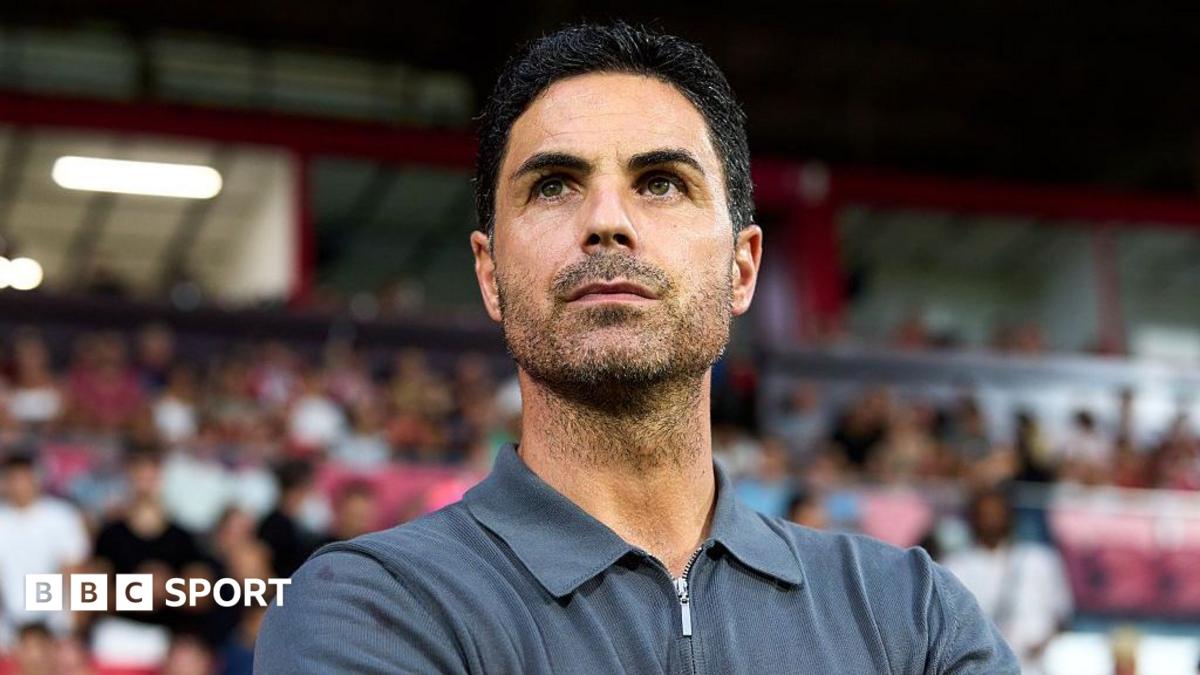 Man in grey polo shirt standing with arms crossed in front of a blurred crowd