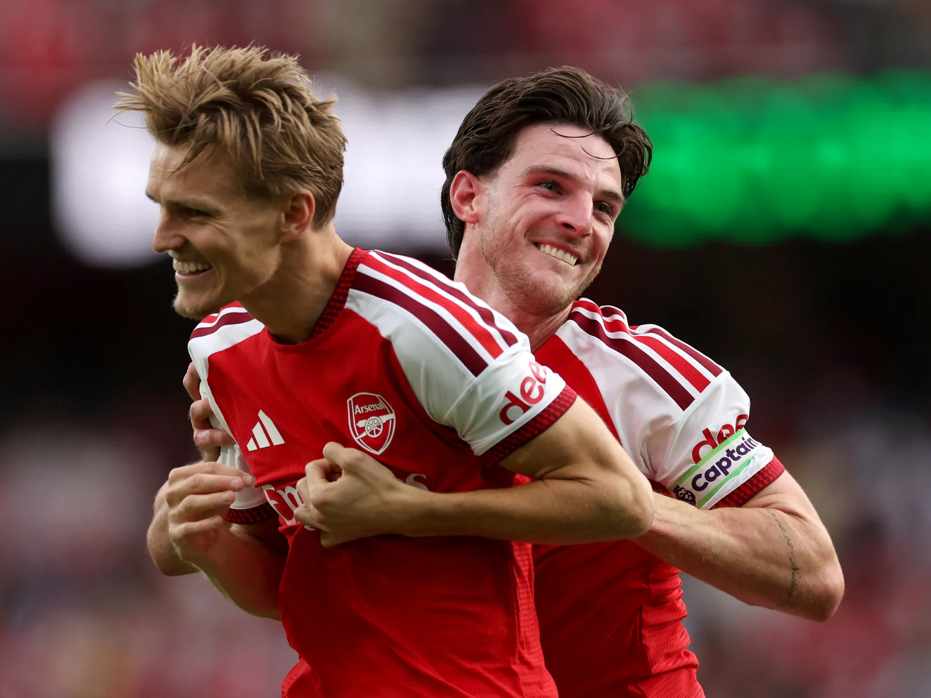 Two Arsenal footballers in red shirts embrace and smile during a match celebration.