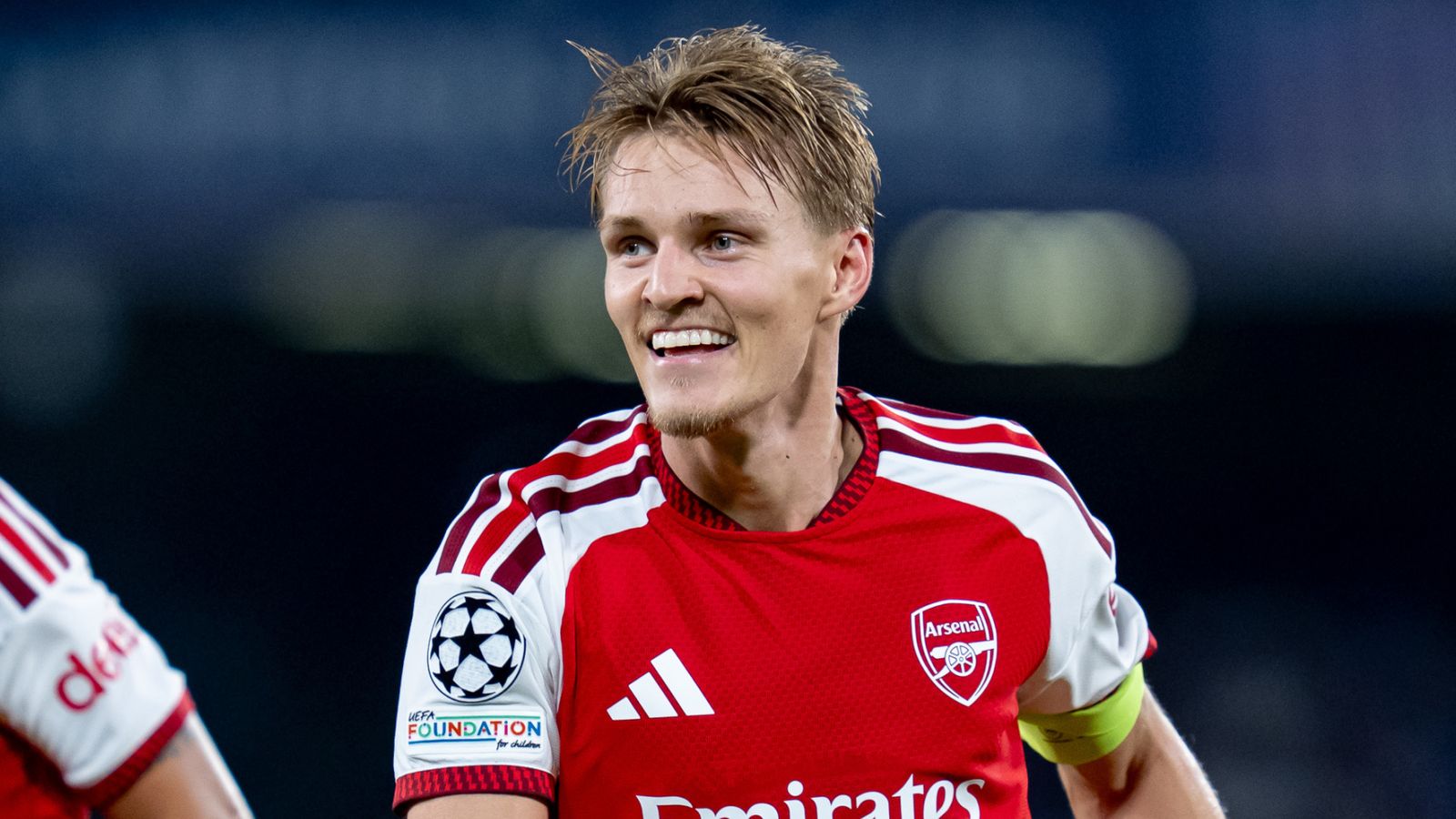 Smiling footballer in an Arsenal jersey wearing a captain’s armband during a match.