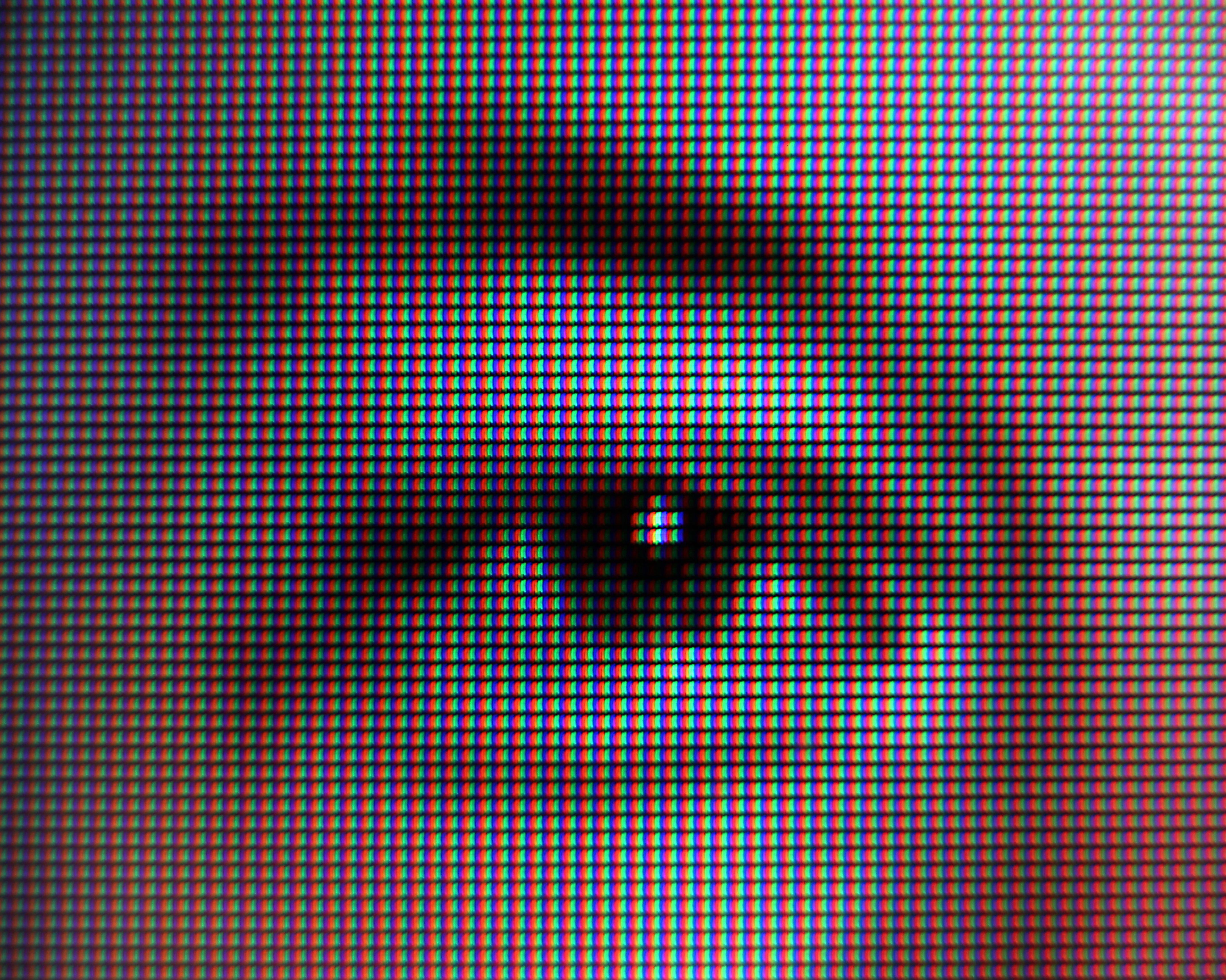 Extreme close-up of a colorful RGB screen pattern with dark, blurry shapes reflected across it.