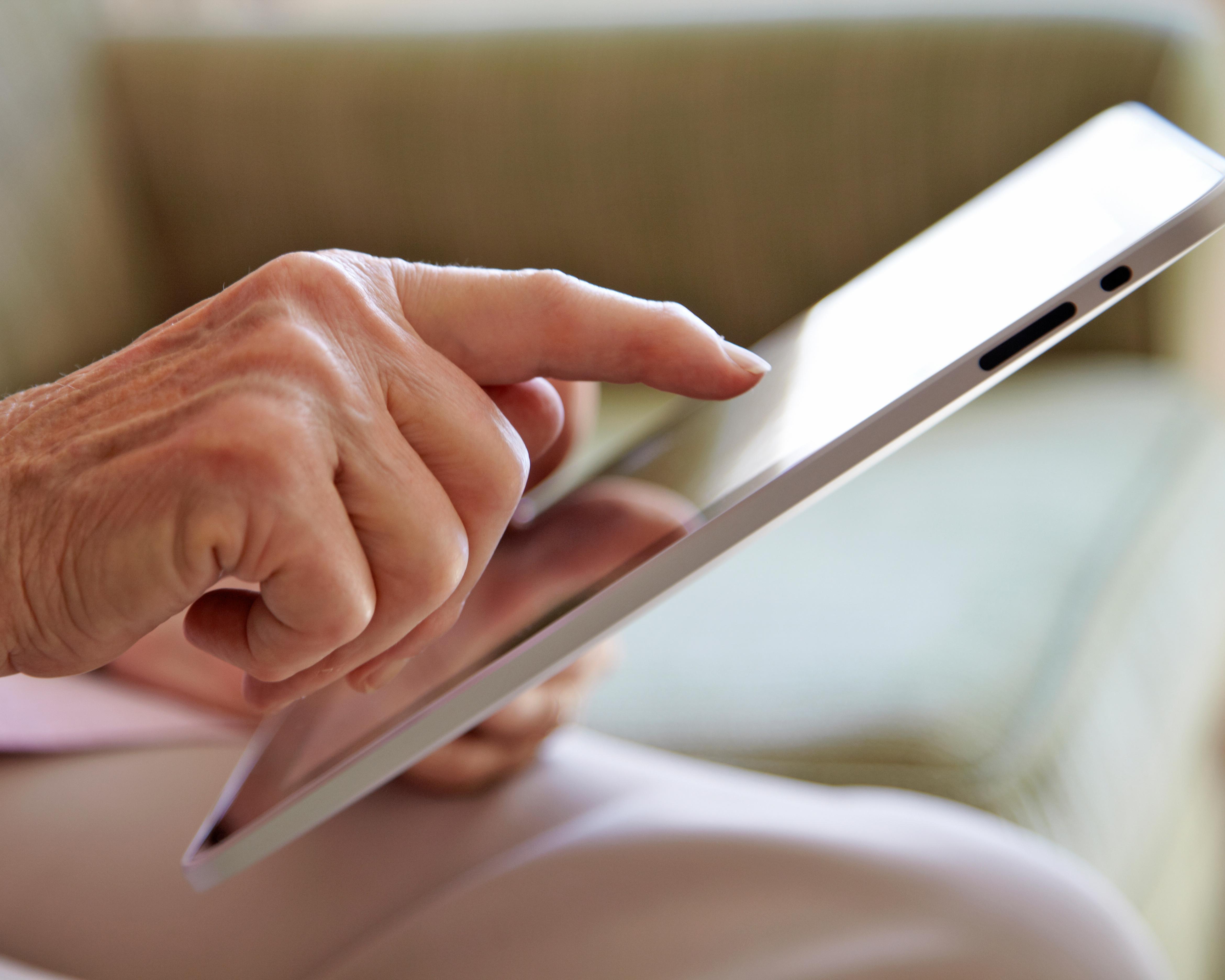 Close-up of a hand reaching toward a tablet with a bright screen