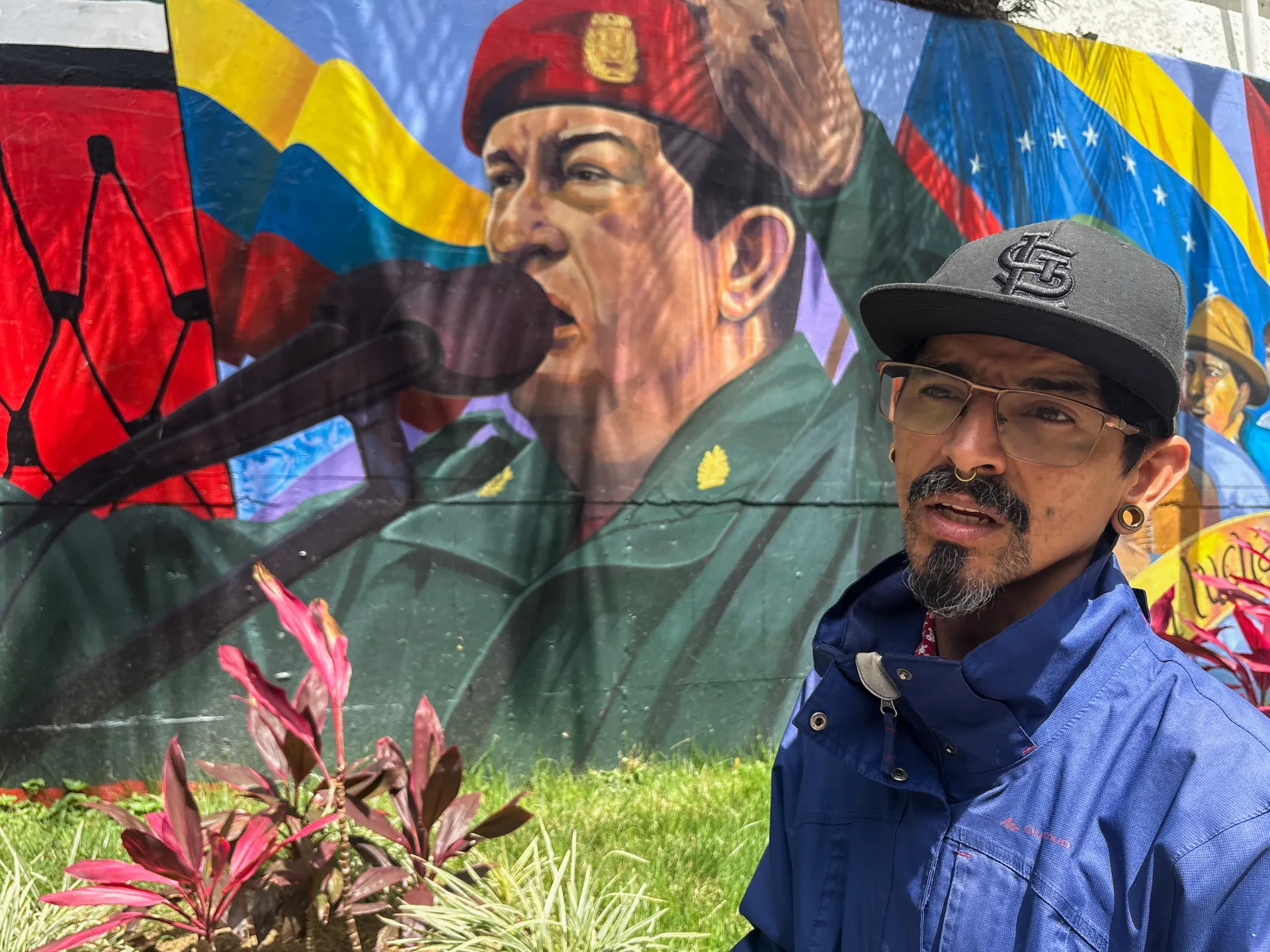 Man poses before a mural depicting a military figure and Venezuelan flags.