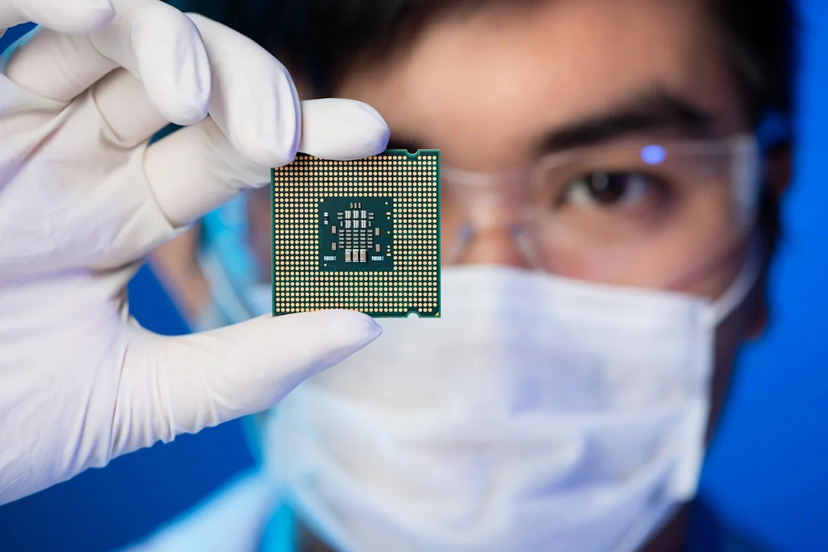 Gloved researcher holds a semiconductor processor chip in front of a masked laboratory worker