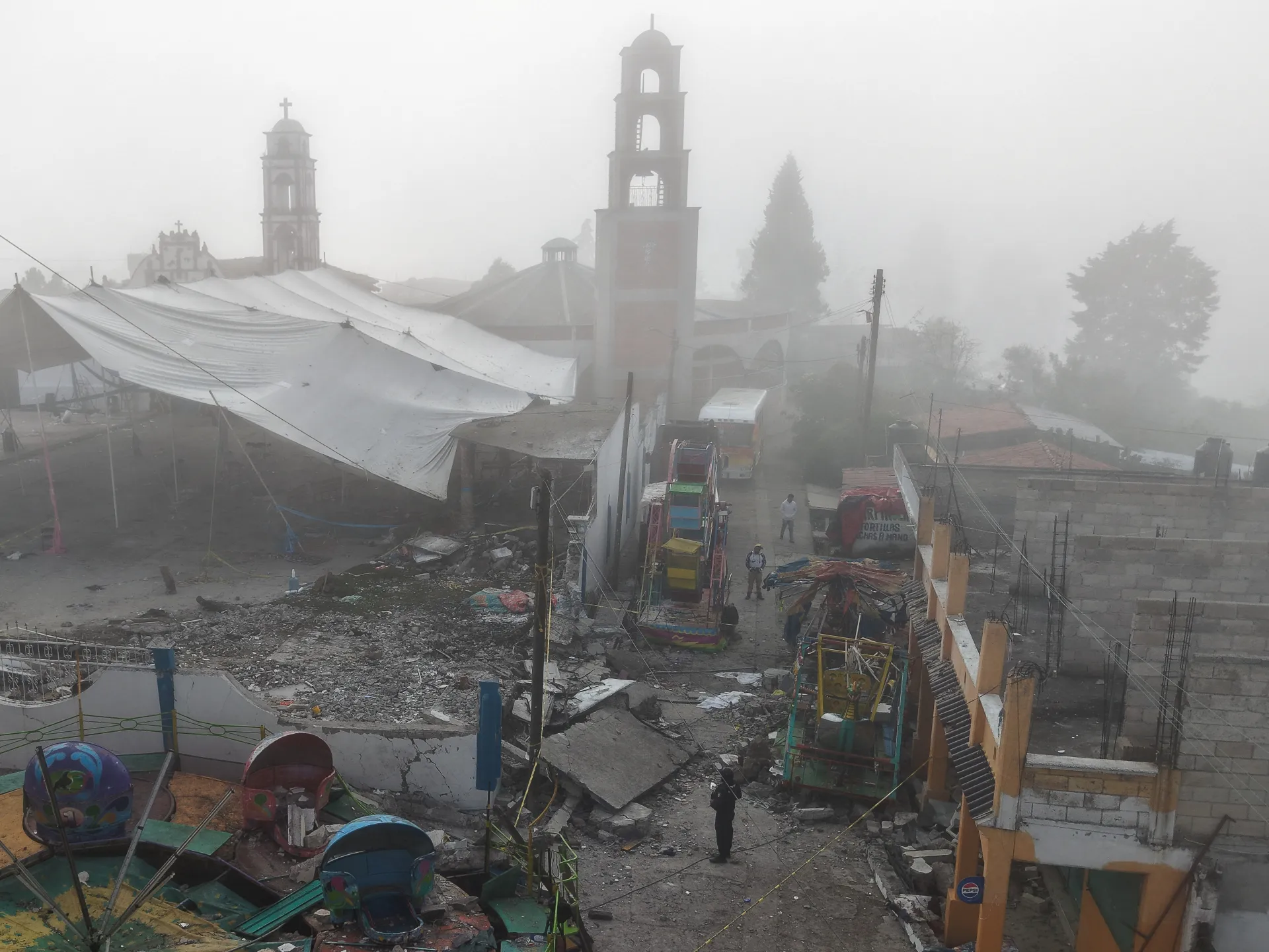 Fog-shrouded church towers overlook a damaged festival area with debris, stalls, and amusement rides.