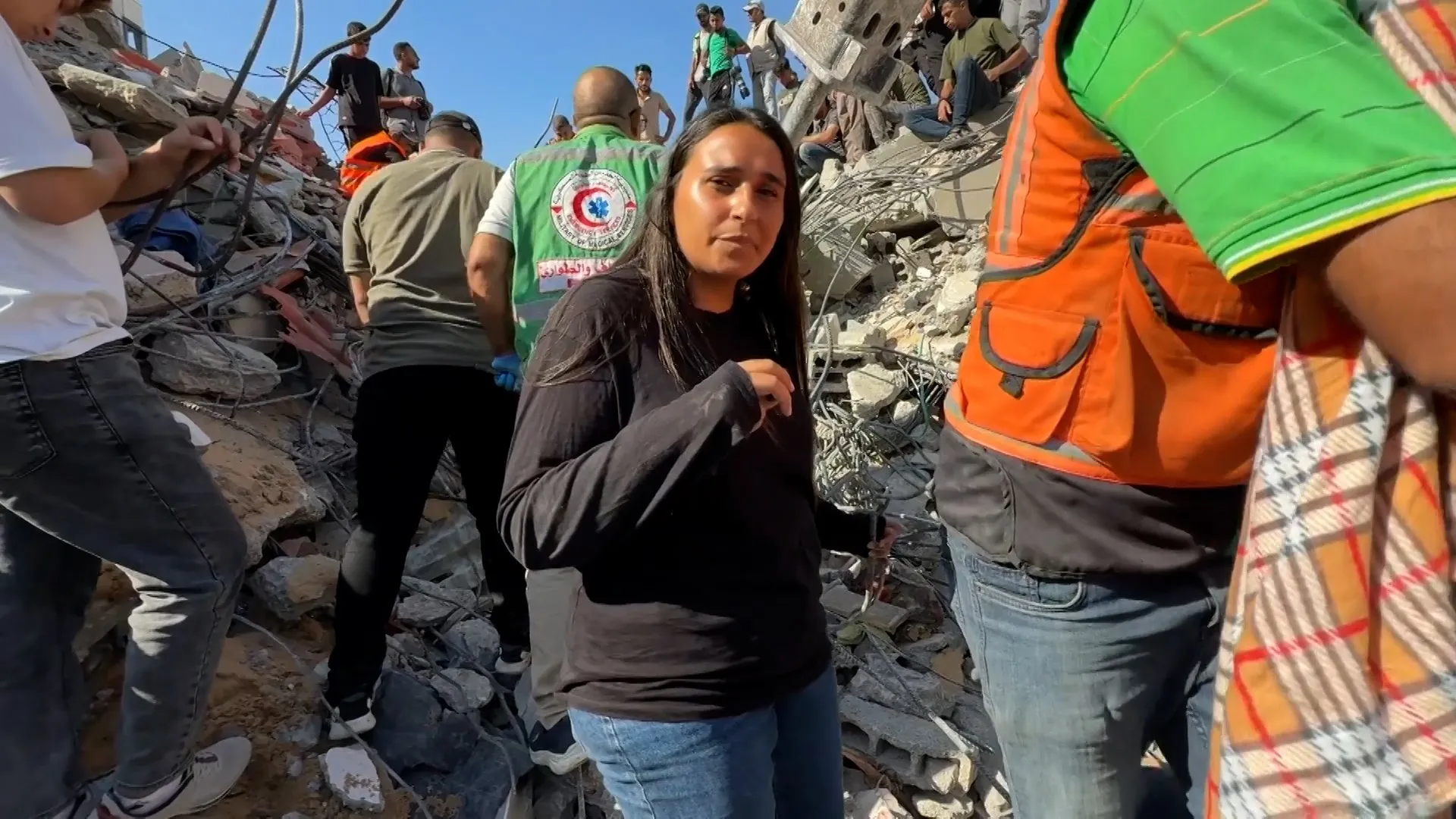 Woman stands amid rubble as rescue workers search a collapsed building site