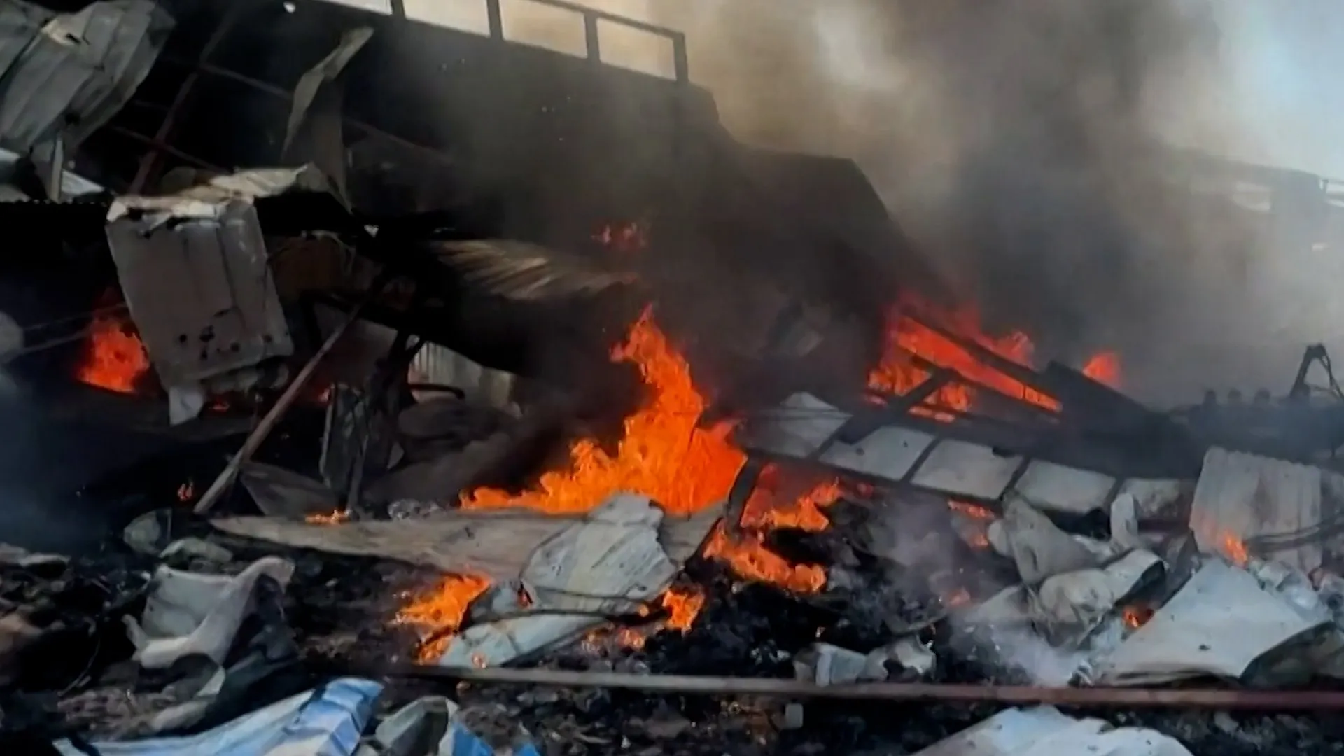 Flames burn amid collapsed market debris as thick smoke fills the damaged structure.