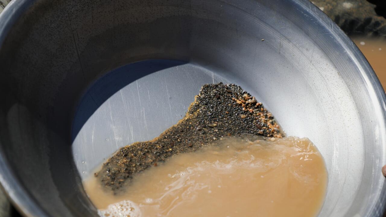 Metal pan holding muddy water and dark sediment with small reddish rocks