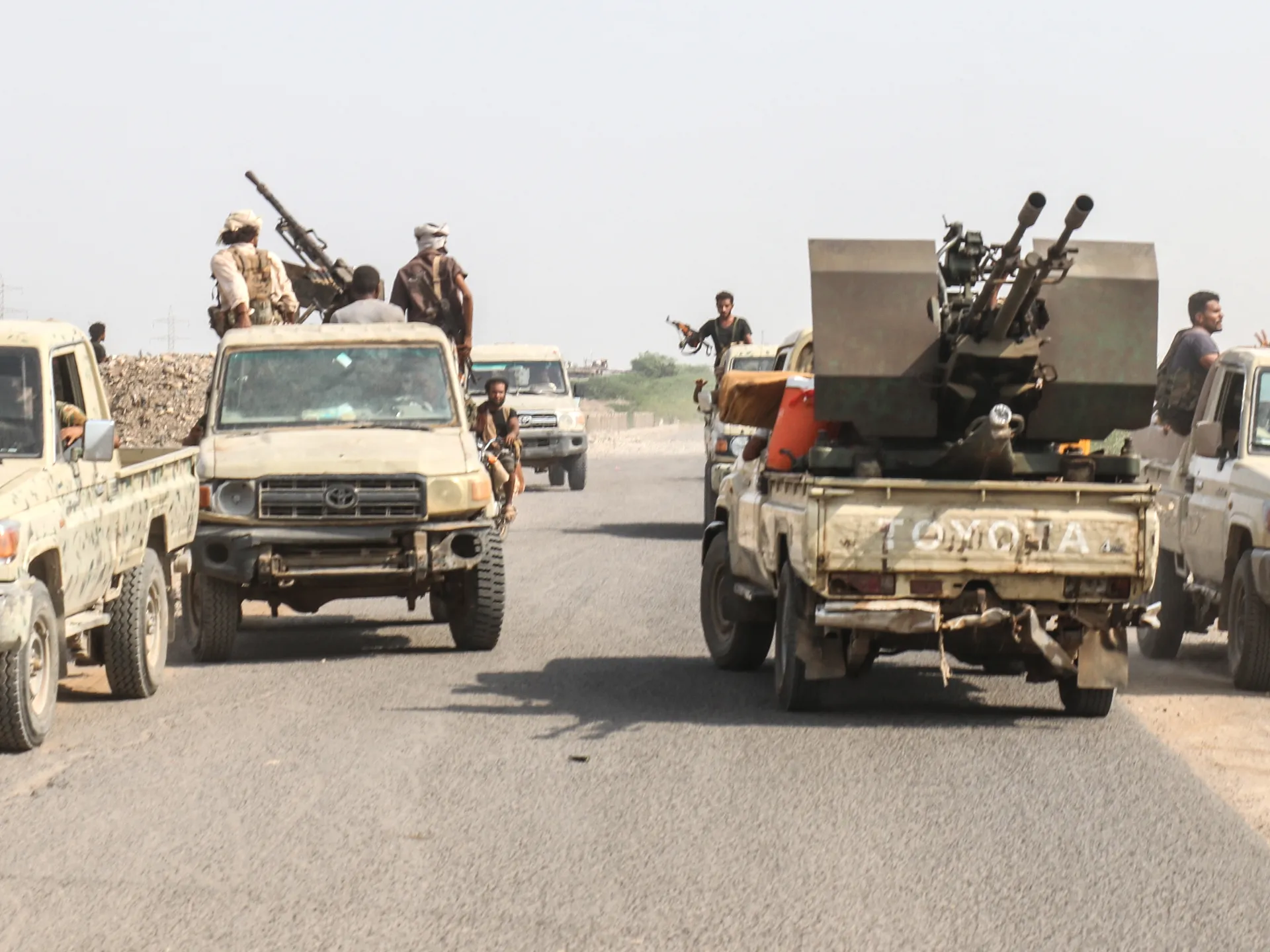 Armed men ride in pickup trucks, including one carrying a mounted twin-barrel weapon.
