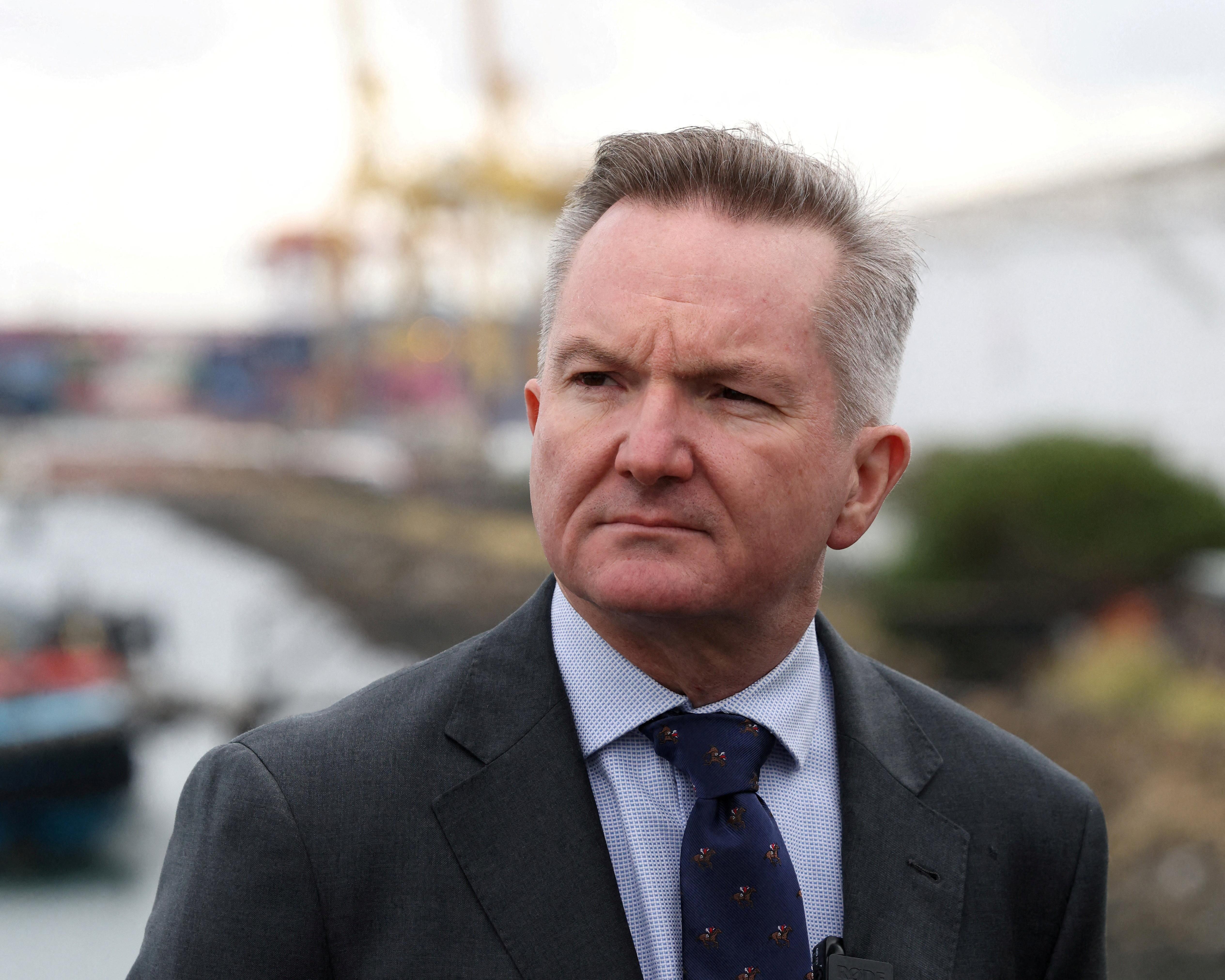 Grey-haired man in a dark suit and patterned tie looks away from camera outdoors