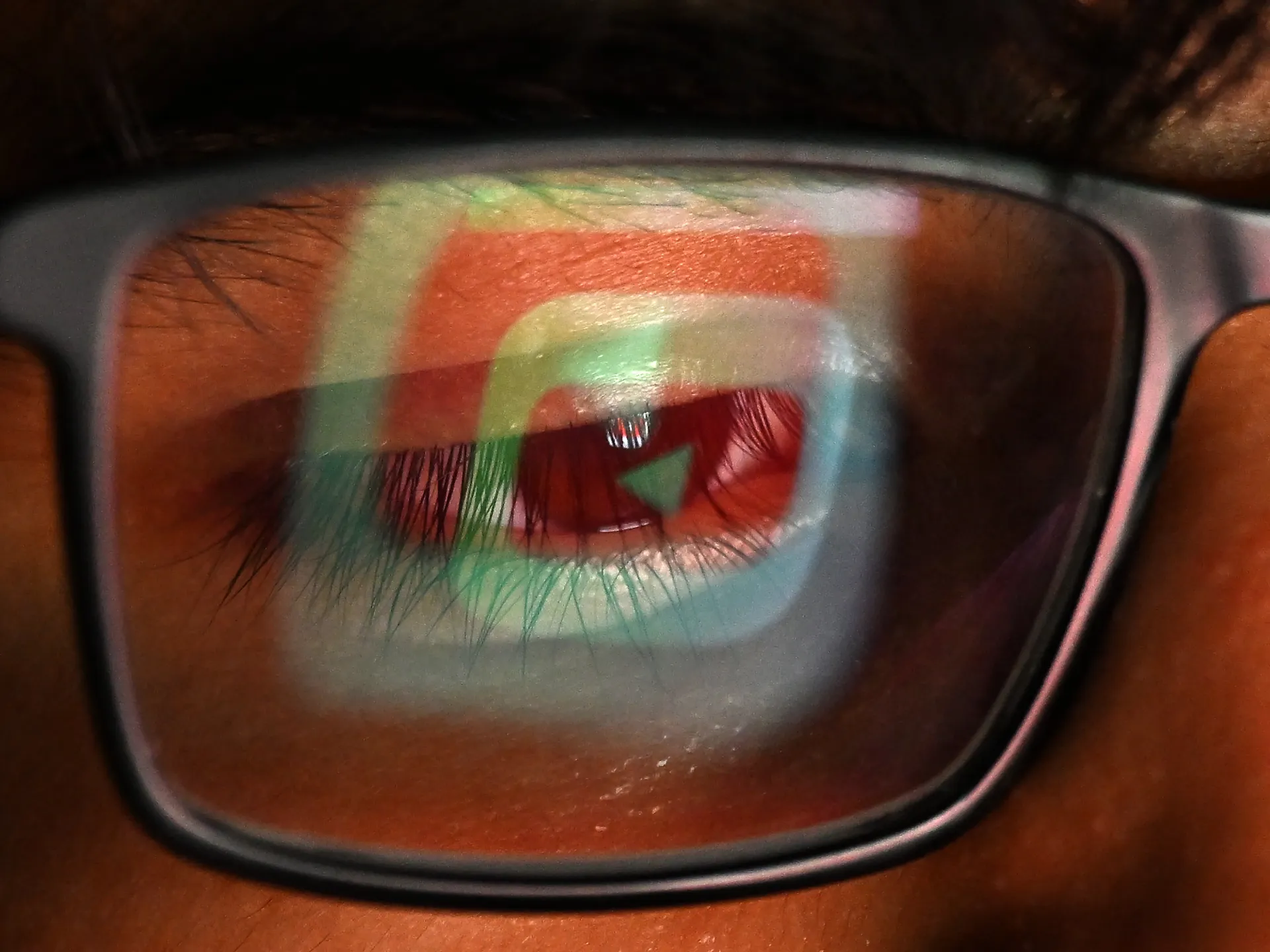 Close-up of an eye seen through eyeglasses reflecting colorful geometric shapes and a play button