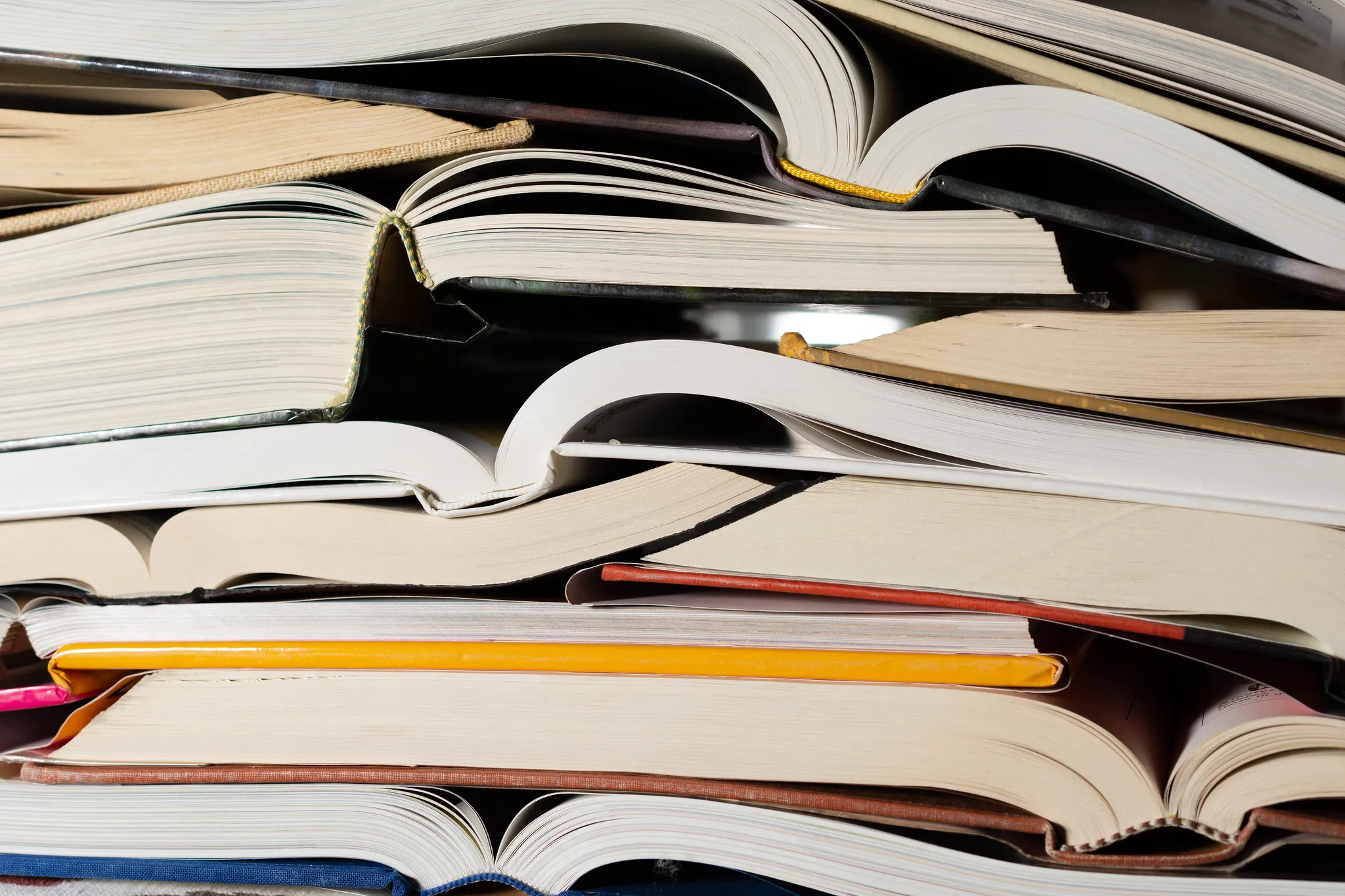 Stack of open and closed books with pages and colorful covers filling the frame.