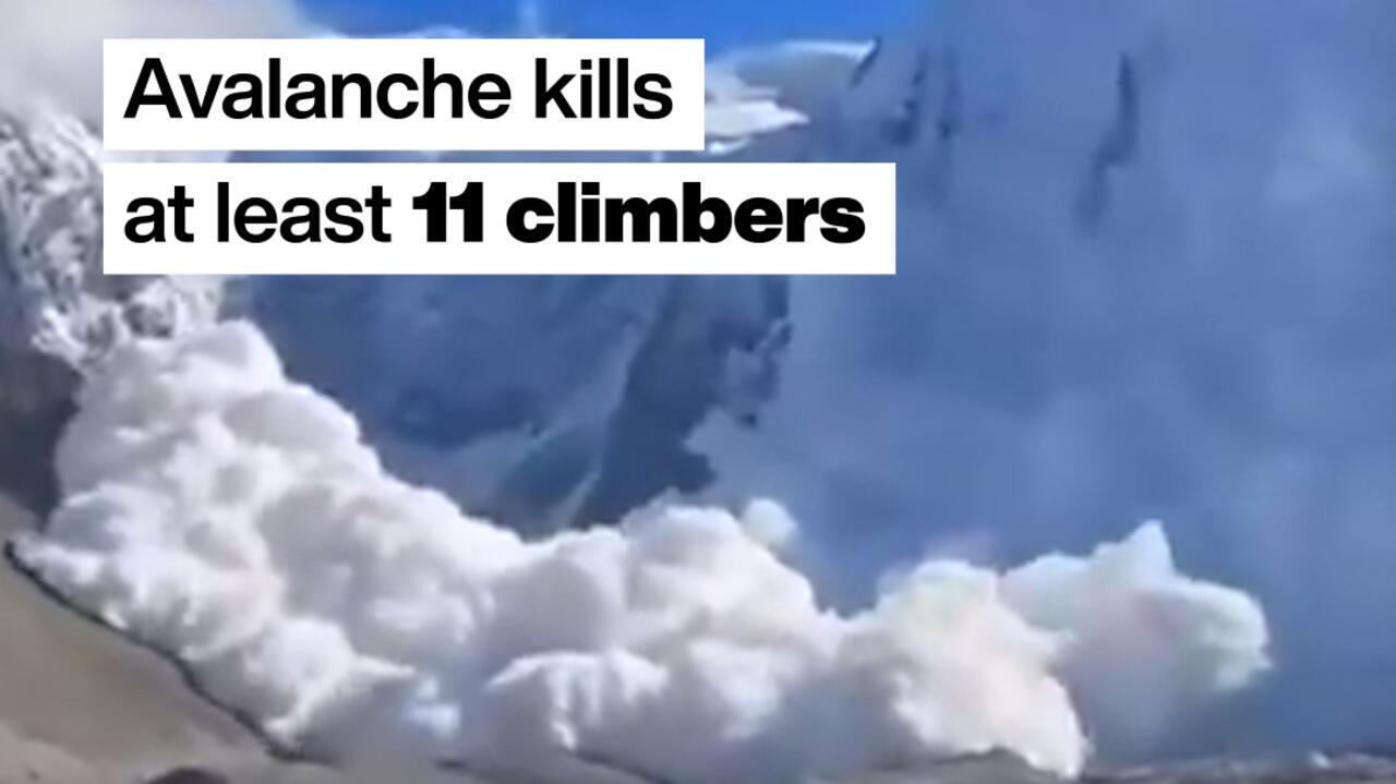 Snow avalanche cascading down a mountain slope beneath a blue sky.