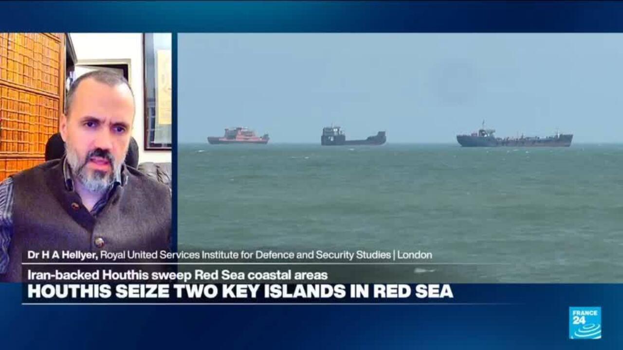 News broadcast shows a bearded analyst beside three cargo ships at sea.