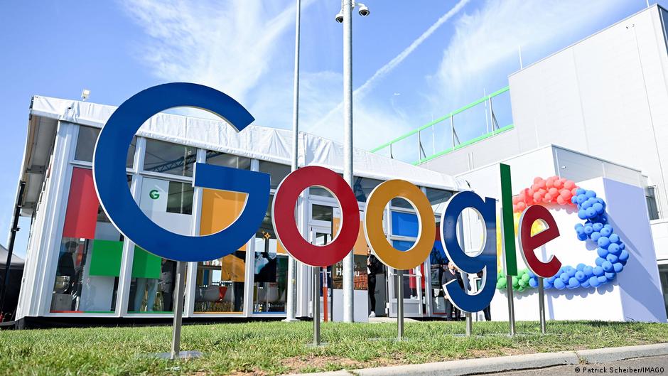 Large multicolored Google letters stand outside a modern building beneath a bright blue sky.