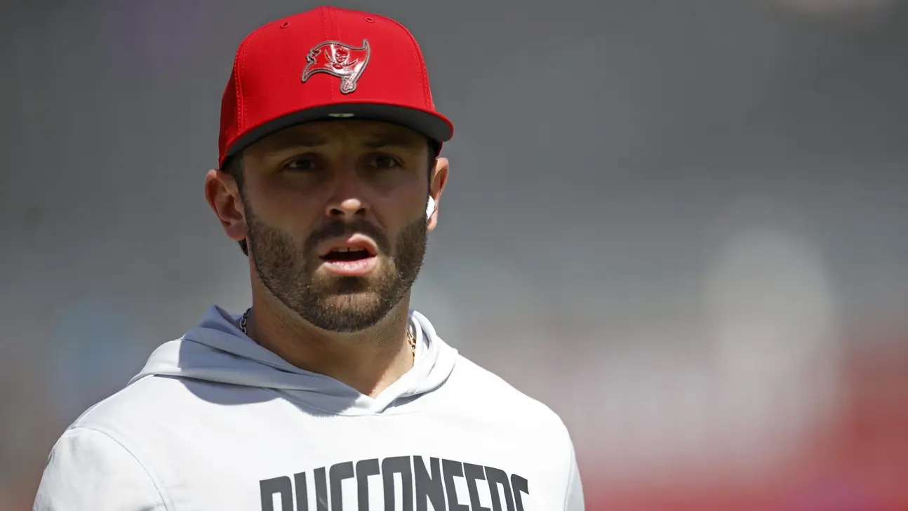 Man wearing a red Buccaneers cap and white hoodie stands against a blurred background.