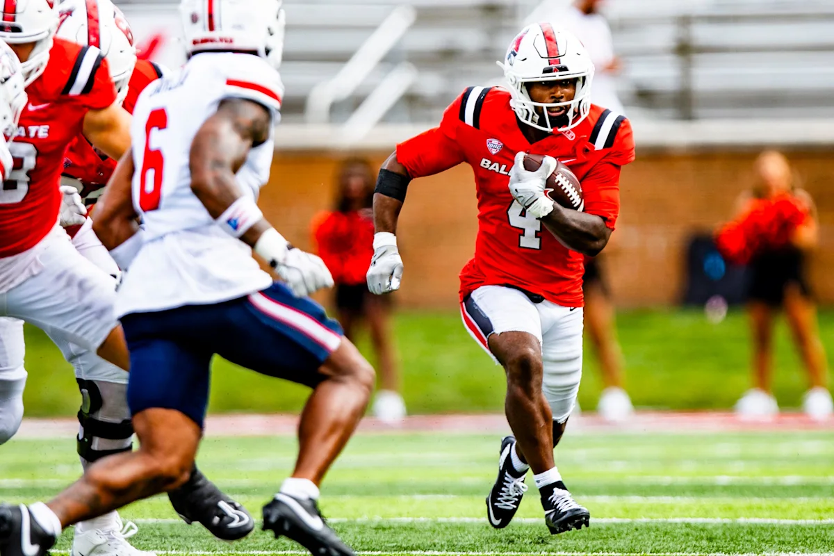Ball State football player in red runs with the ball as defenders pursue.