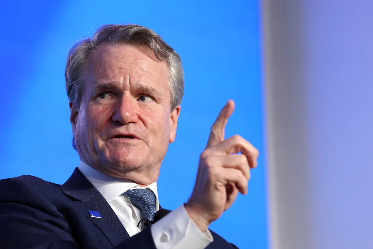Gray-haired man in suit gestures with raised finger against a bright blue backdrop