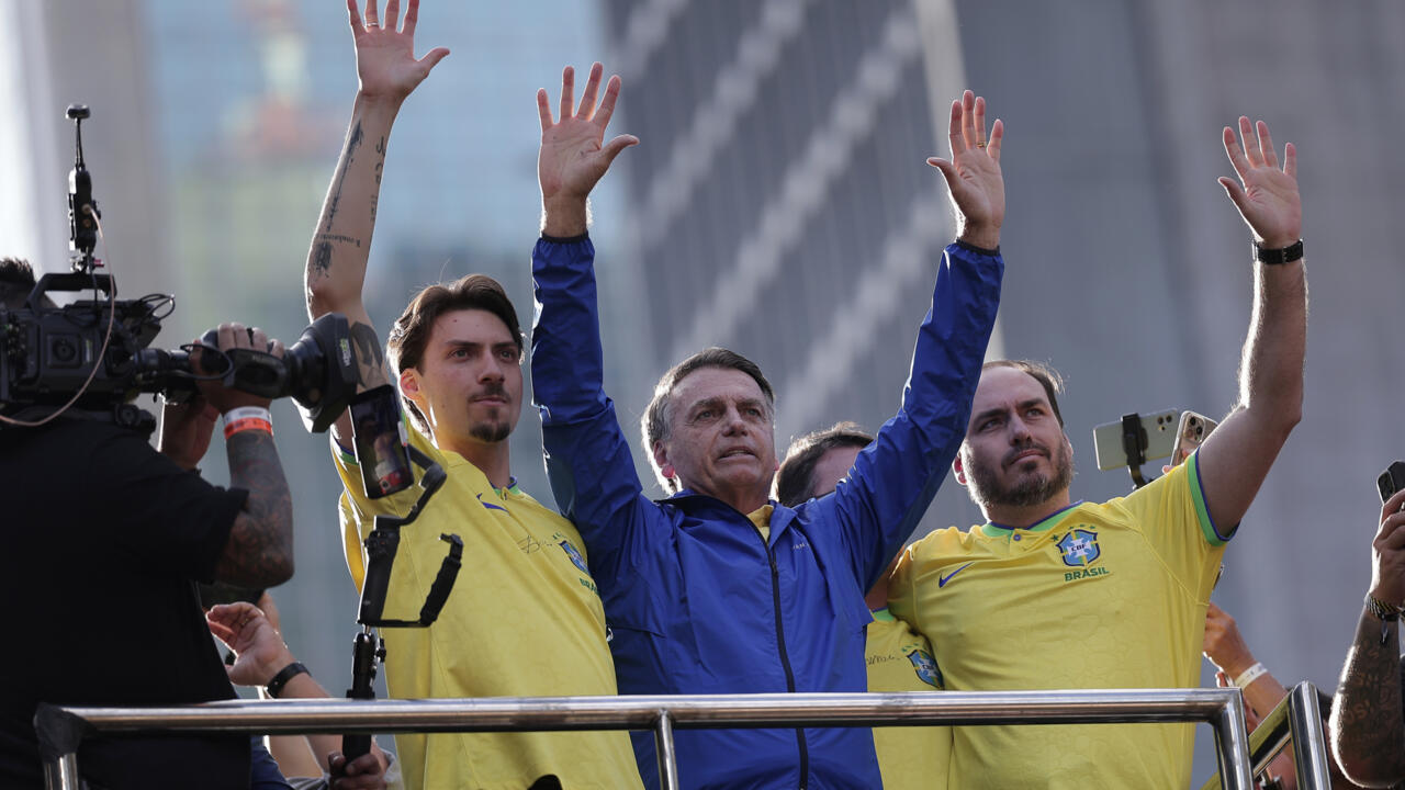 Three men, including a central politician, raise their hands beside supporters in Brazil-themed yellow shirts.