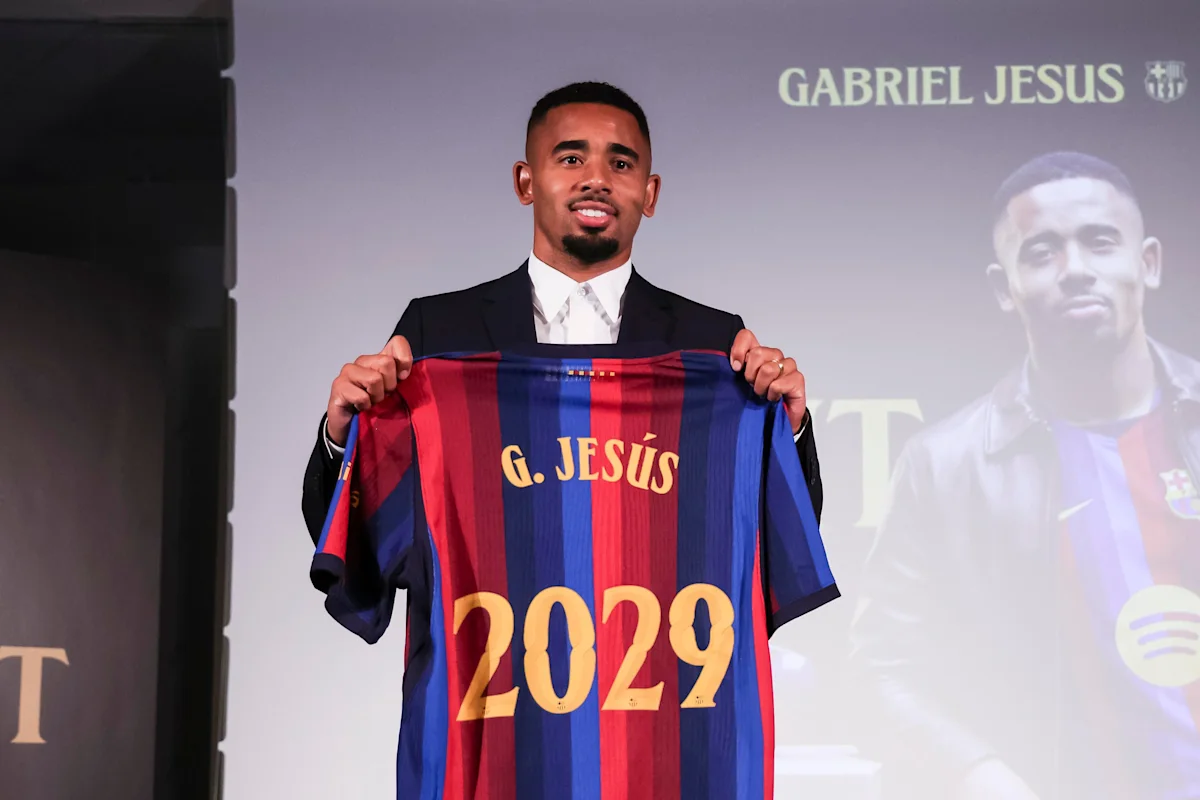 Man in suit holds up a Barcelona jersey displaying G. Jesús and 2029.