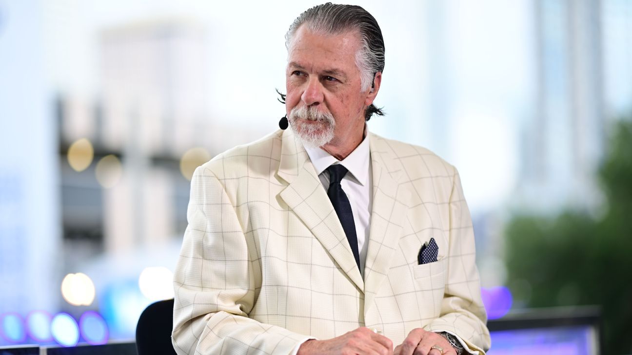 Gray-haired man in a cream checked suit and dark tie seated wearing a headset