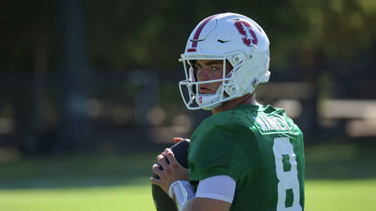 A football player in a green jersey and white helmet holds a ball during practice.