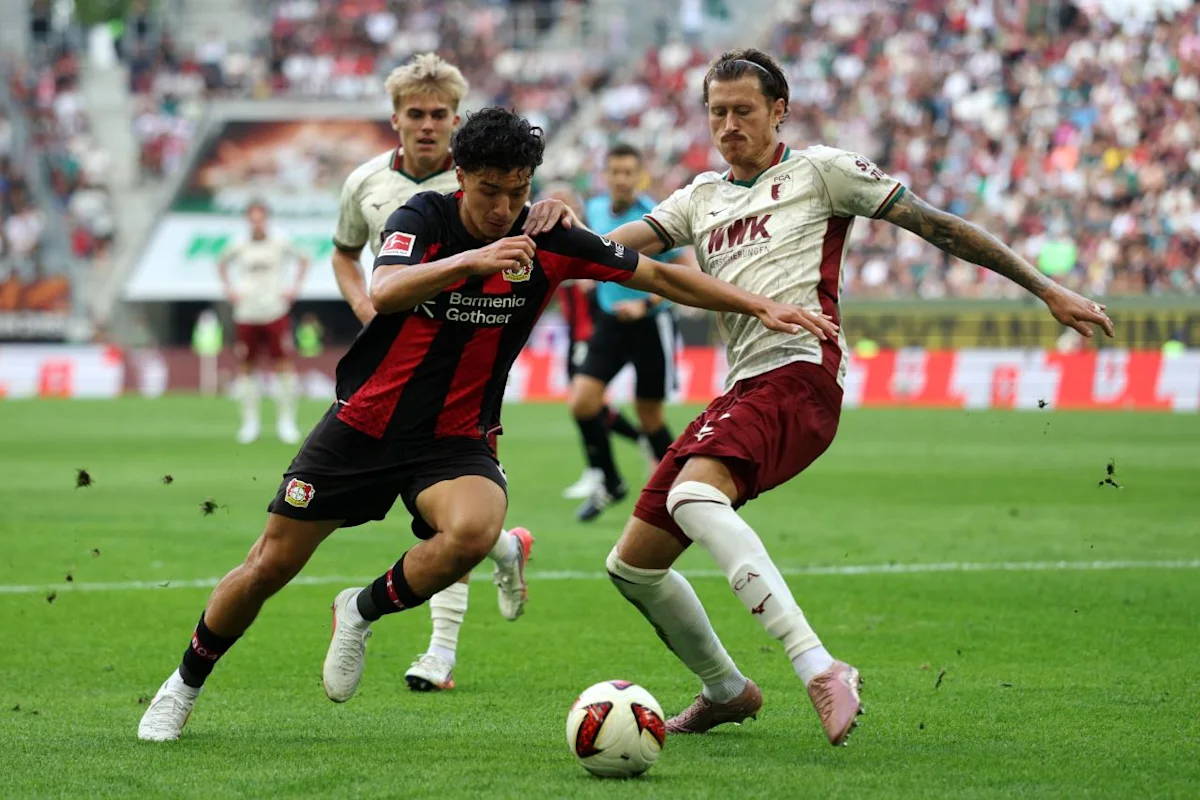 Bayer Leverkusen player challenges an Augsburg opponent for the ball during a football match.
