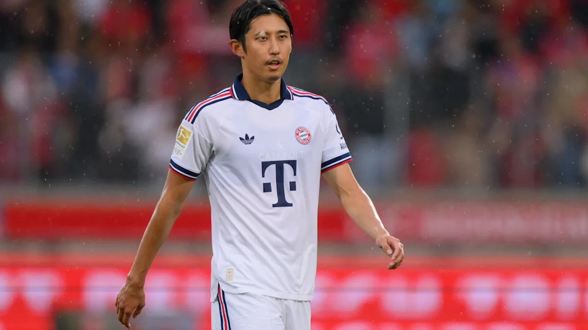 Footballer in a white Bayern Munich kit stands on the pitch during a match.