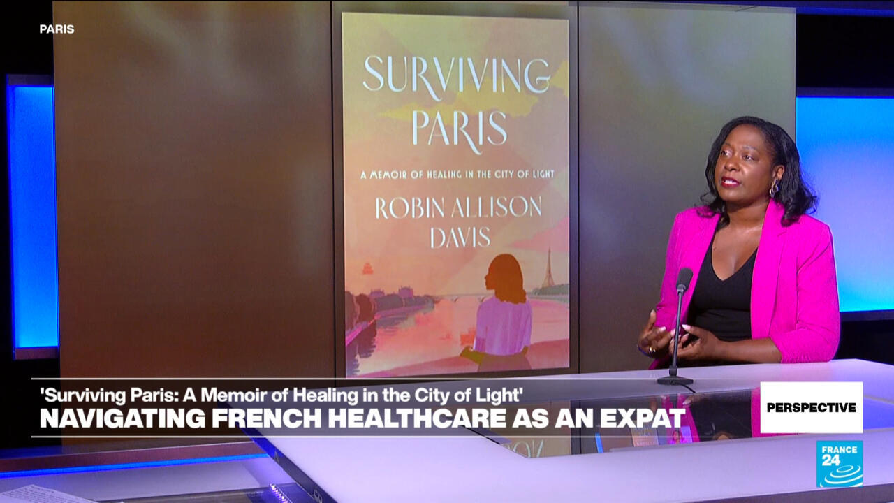 Woman in pink blazer speaks beside a projected book cover in a television studio.