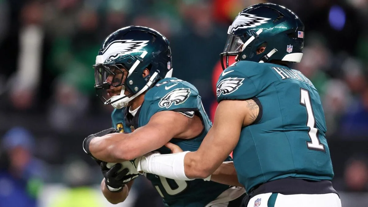 Two Philadelphia Eagles players in teal uniforms and helmets handle the football during a game.