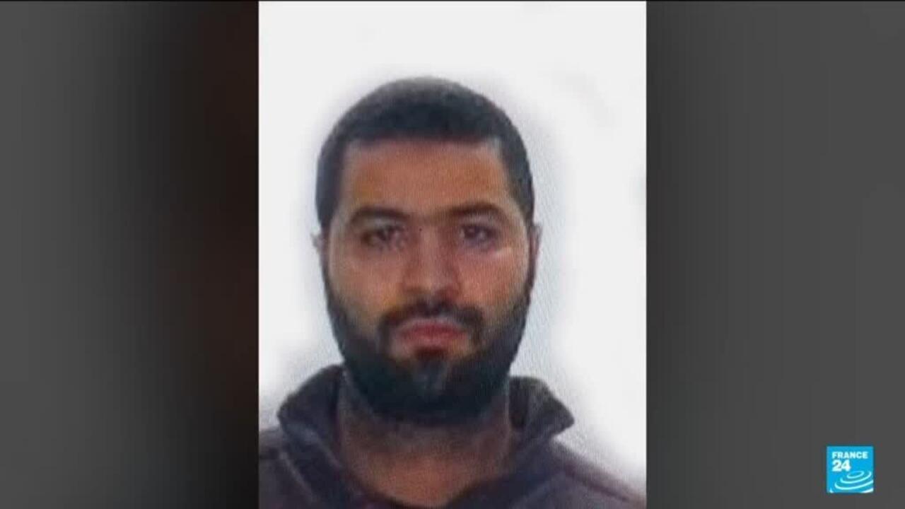 Portrait of a bearded man wearing a dark hooded top against a light background