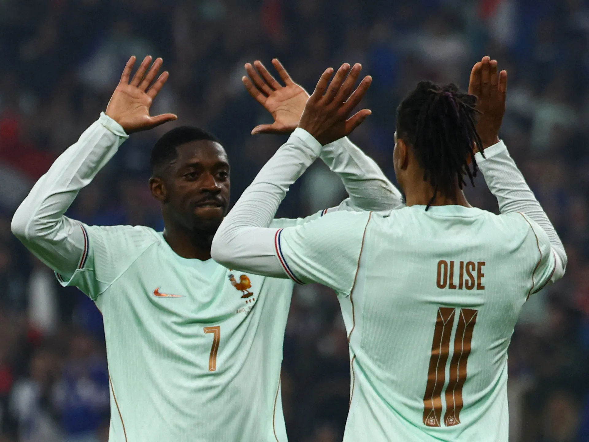 Two footballers in white France shirts raise their hands to high-five, one seen from behind wearing Olise number 11.