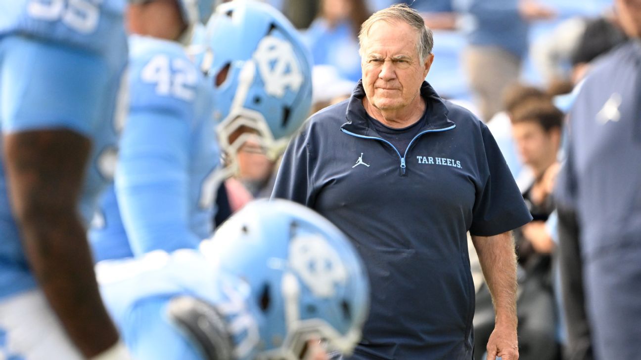 Older man in North Carolina Tar Heels sweatshirt walking among football players wearing helmets