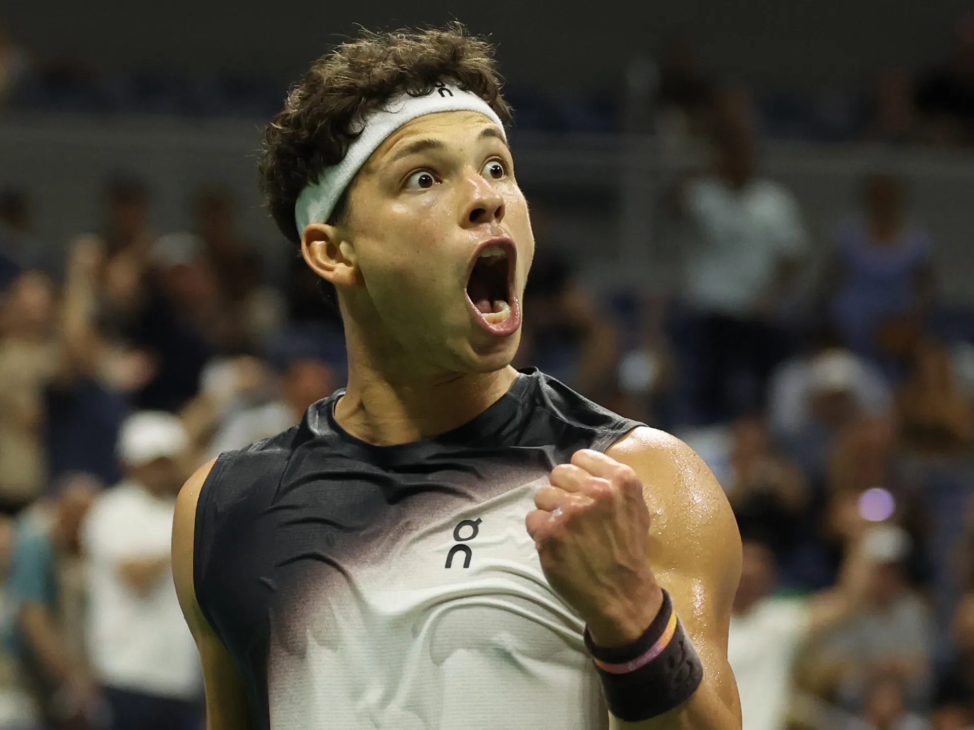 Tennis player in headband celebrates with clenched fist and mouth open during a match