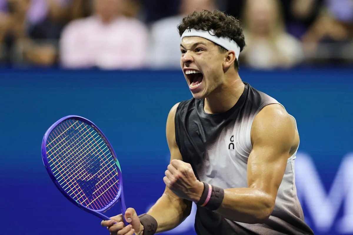 Tennis player wearing a white headband celebrates while gripping a racket during a match.