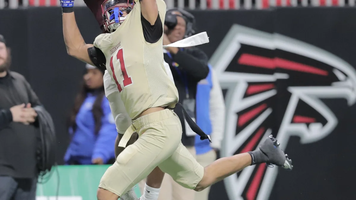 Football player in cream number 11 uniform celebrates with arms raised in front of an Atlanta Falcons logo.