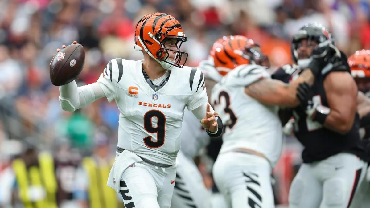 Bengals quarterback in a white uniform prepares to throw as players block defenders during a football game.